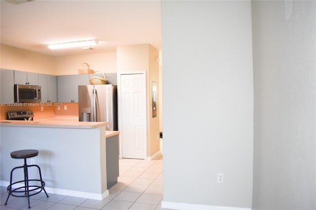 9123 SW 152nd Path, Miami, FL 33196 - kitchen featuring appliances with stainless steel finishes, light tile patterned floors, gray cabinets, a breakfast bar area, and a peninsula