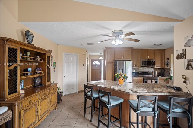 15824 Cotswold Ct, Davie, FL 33331 - kitchen with stainless steel appliances, a peninsula, a kitchen bar, light tile patterned flooring, and tasteful backsplash