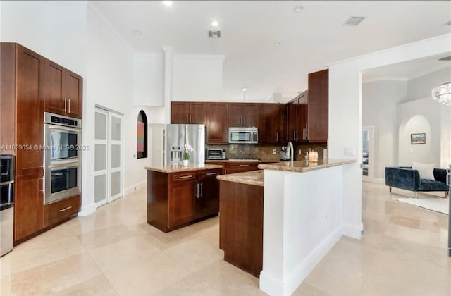 14095 NW 22nd Ct, Pembroke Pines, FL 33028 - kitchen featuring appliances with stainless steel finishes, arched walkways, decorative backsplash, light stone countertops, and a kitchen island