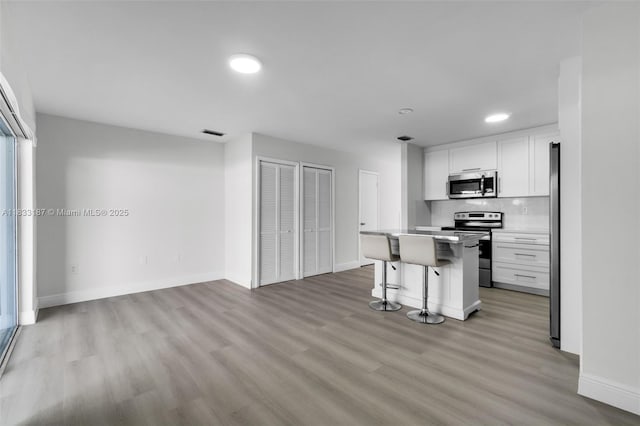 6514 SW 128th Pl Unit 6514, Miami, FL 33183 - kitchen with stainless steel appliances, a breakfast bar, white cabinets, light wood finished floors, and backsplash