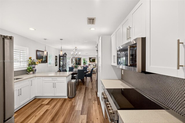 240 NE 97th St, Miami Shores, FL 33138 - kitchen featuring stainless steel appliances, light wood finished floors, light countertops, a chandelier, and white cabinets