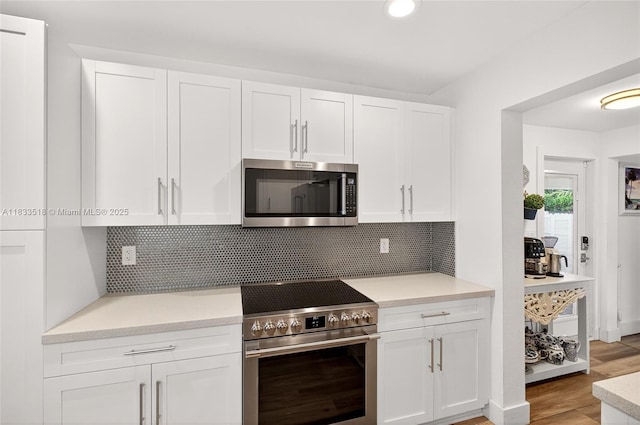 240 NE 97th St, Miami Shores, FL 33138 - kitchen featuring stainless steel appliances, white cabinets, light countertops, light wood-style flooring, and backsplash