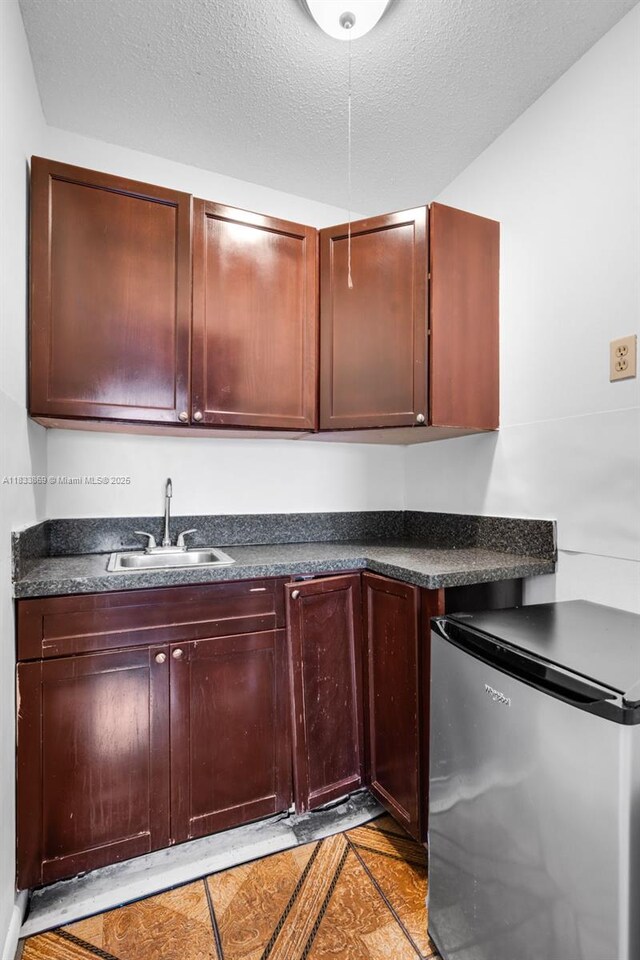 2727 Hypoluxo Rd, Boynton Beach, FL 33462 - kitchen featuring freestanding refrigerator, dark countertops, dark brown cabinets, a textured ceiling, and light tile patterned flooring