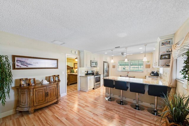 841 Meadowlark Ln, Delray Beach, FL 33445 - kitchen with stainless steel appliances, light wood-style floors, a peninsula, decorative backsplash, and a kitchen bar