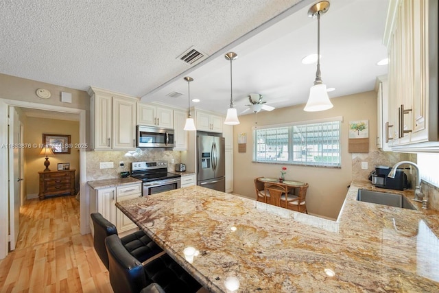 841 Meadowlark Ln, Delray Beach, FL 33445 - kitchen featuring appliances with stainless steel finishes, a peninsula, light stone counters, light wood-style floors, and tasteful backsplash