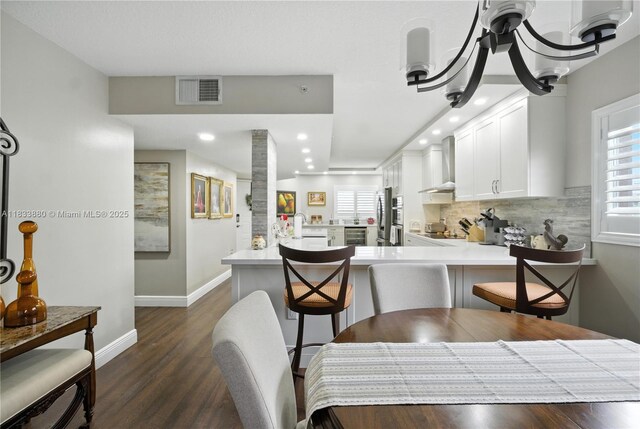 1651 SW 127th Ave Unit 301A, Pembroke Pines, FL 33027 - kitchen featuring wall chimney exhaust hood, a peninsula, tasteful backsplash, white cabinets, and dark wood-type flooring