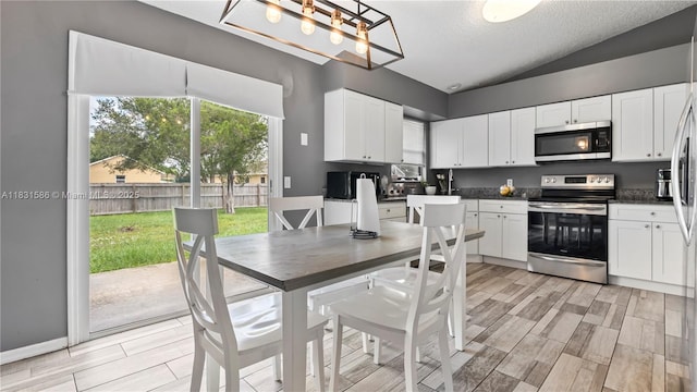 1226 SW Curry St, Port St Lucie, FL 34983 - kitchen with appliances with stainless steel finishes, lofted ceiling, white cabinetry, dark countertops, and wood finish floors