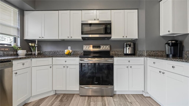 1226 SW Curry St, Port St Lucie, FL 34983 - kitchen with appliances with stainless steel finishes, white cabinets, light wood finished floors, and dark stone counters