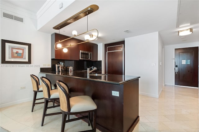 4391 Collins Ave Unit 623, Miami Beach, FL 33140 - kitchen featuring stainless steel microwave, dark countertops, a peninsula, a kitchen breakfast bar, and backsplash
