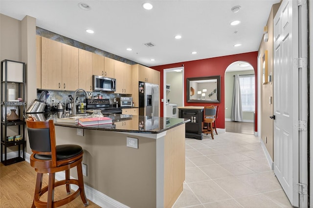 153 Apalachee Ln, Jupiter, FL 33458 - kitchen with stainless steel appliances, light brown cabinets, a peninsula, washer / clothes dryer, and a breakfast bar area