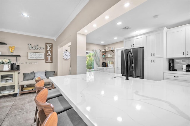 5820 Australian Pine Dr, Tamarac, FL 33319 - kitchen with stainless steel fridge with ice dispenser, crown molding, white cabinets, a breakfast bar, and light stone counters
