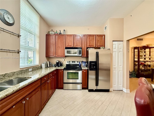 3001 NE 185th St Unit 112, Aventura, FL 33180 - kitchen featuring appliances with stainless steel finishes, light stone counters, a textured ceiling, light wood finished floors, and brown cabinetry