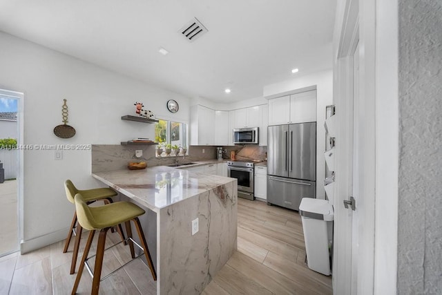 985 SW 147th Ct, Miami, FL 33194 - kitchen featuring stainless steel appliances, a peninsula, white cabinetry, light stone countertops, and a breakfast bar