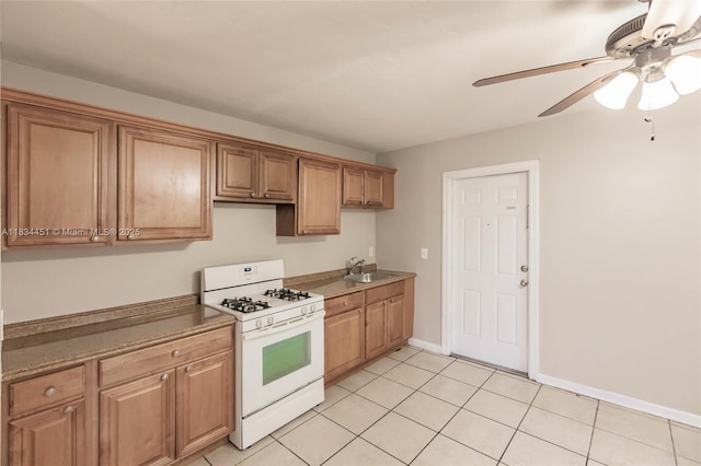 4423 Lake Ave, West Palm Beach, FL 33405 - kitchen featuring white gas range, light tile patterned floors, ceiling fan, and brown cabinetry
