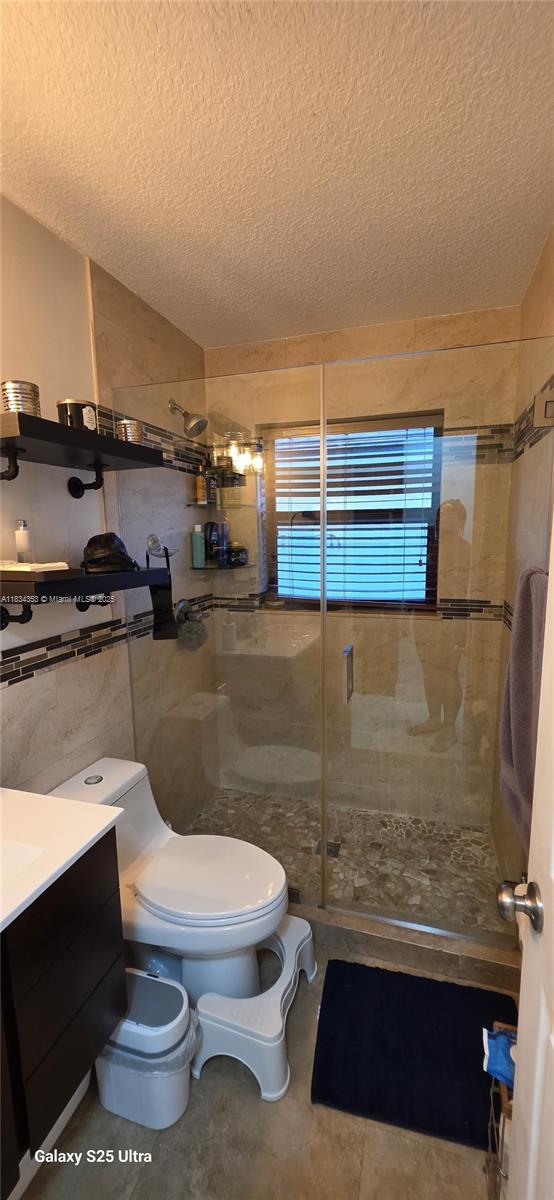 19185 SW 25th Ct, Miramar, FL 33029 - full bath featuring a textured ceiling, a shower stall, vanity, and tile walls