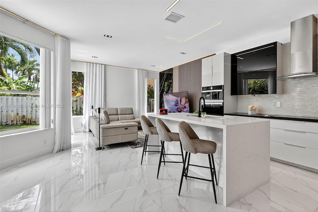 2036 SW 159th Ave, Miramar, FL 33027 - kitchen featuring modern cabinets, wall chimney range hood, light marble finish flooring, tasteful backsplash, and a breakfast bar