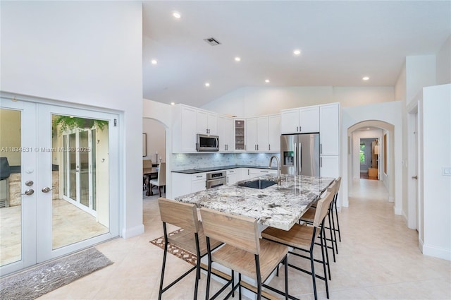 1583 SW 191st Ave, Pembroke Pines, FL 33029 - kitchen featuring appliances with stainless steel finishes, arched walkways, white cabinetry, a kitchen bar, and high vaulted ceiling