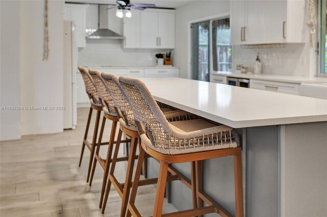 7735 Edgewater Dr, Lake Clarke Shores, FL 33406 - kitchen featuring wall chimney exhaust hood, light countertops, tasteful backsplash, a kitchen breakfast bar, and white cabinetry