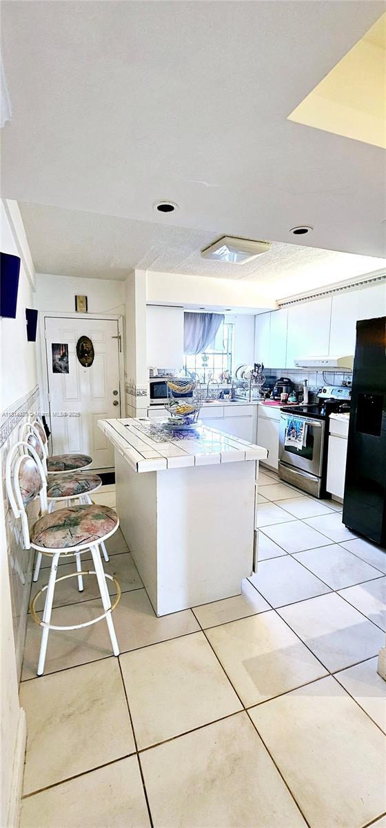 3494 E 4th Ave Unit 1207, Hialeah, FL 33013 - kitchen with stainless steel electric stove, white cabinets, light countertops, black refrigerator with ice dispenser, and light tile patterned flooring