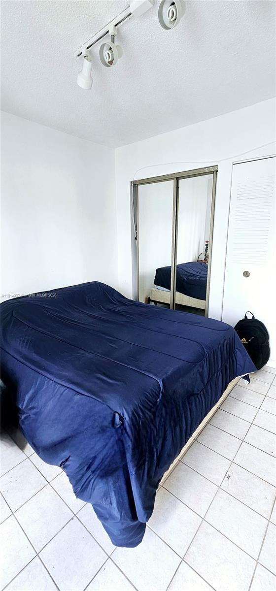 3494 E 4th Ave Unit 1207, Hialeah, FL 33013 - bedroom featuring light tile patterned floors, rail lighting, a textured ceiling, and a closet