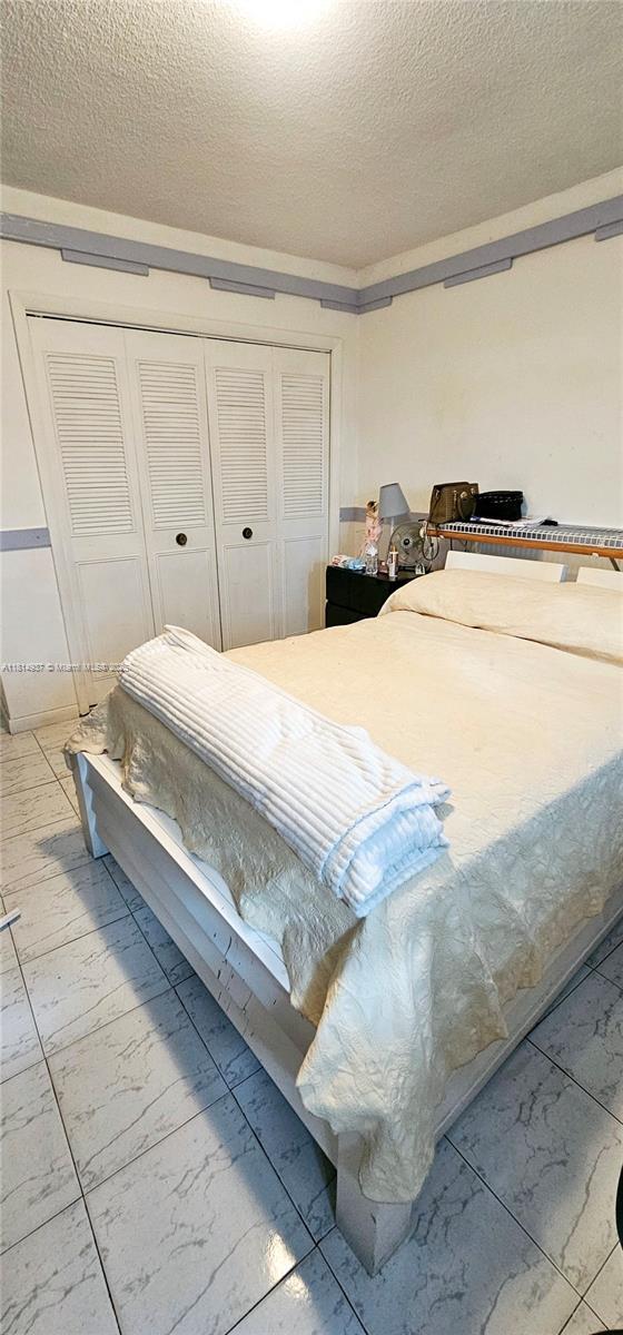 3494 E 4th Ave Unit 1207, Hialeah, FL 33013 - bedroom with marble finish flooring, a textured ceiling, and a closet