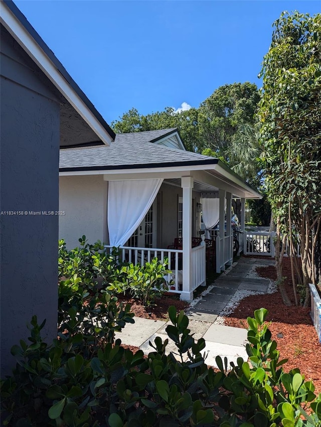 view of side of home with a porch, a shingled roof, and stucco siding
