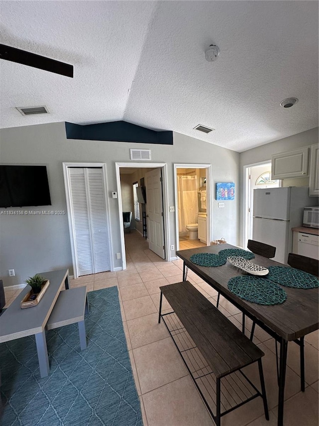 dining room featuring vaulted ceiling, light tile patterned flooring, and a textured ceiling