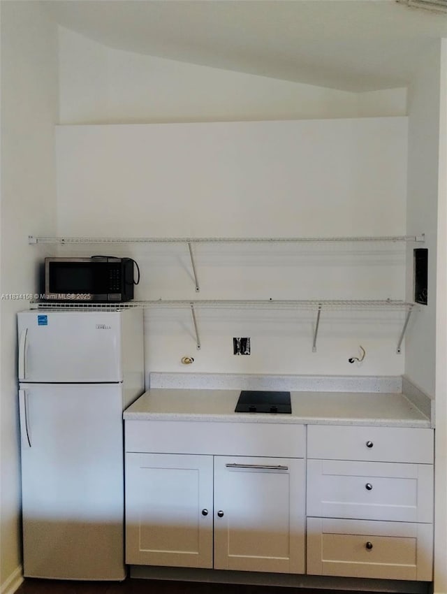 kitchen with freestanding refrigerator, stainless steel microwave, light countertops, and white cabinets