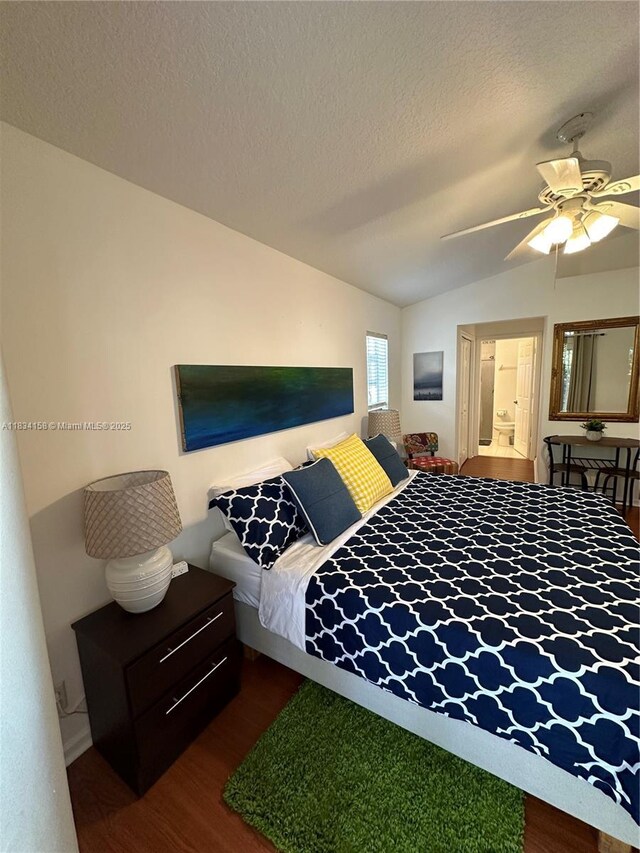 bedroom with wood finished floors, vaulted ceiling, a textured ceiling, a ceiling fan, and connected bathroom