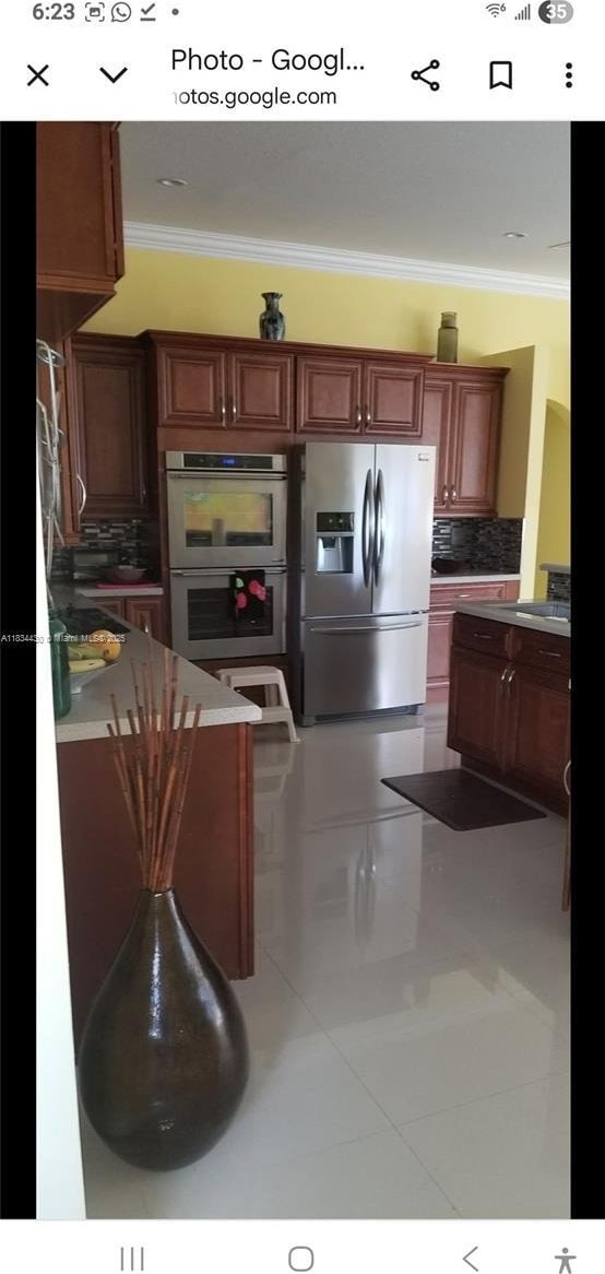 kitchen with appliances with stainless steel finishes, crown molding, tasteful backsplash, and tile patterned floors