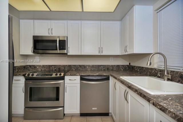 2101 NE 68th St Unit 103, Fort Lauderdale, FL 33308 - kitchen with appliances with stainless steel finishes, white cabinetry, light tile patterned floors, and dark stone counters