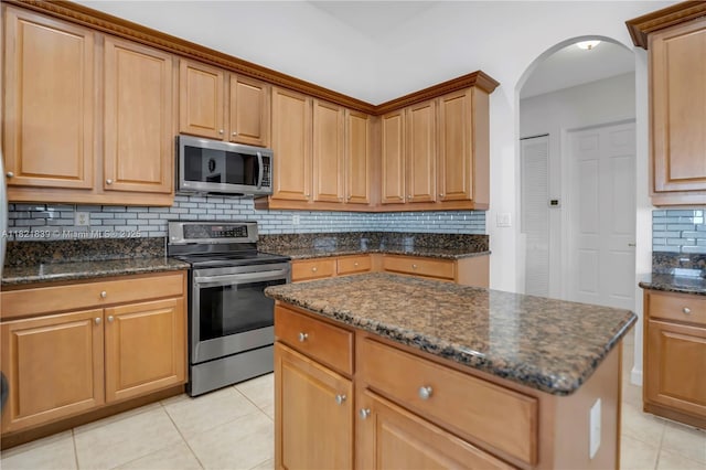 18633 SW 24th St, Miramar, FL 33029 - kitchen featuring stainless steel appliances, light tile patterned floors, backsplash, arched walkways, and dark stone countertops