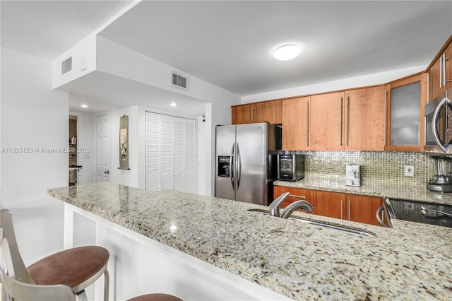 401 Ocean Dr Unit 1024, Miami Beach, FL 33139 - kitchen with appliances with stainless steel finishes, brown cabinets, light stone countertops, and a kitchen breakfast bar