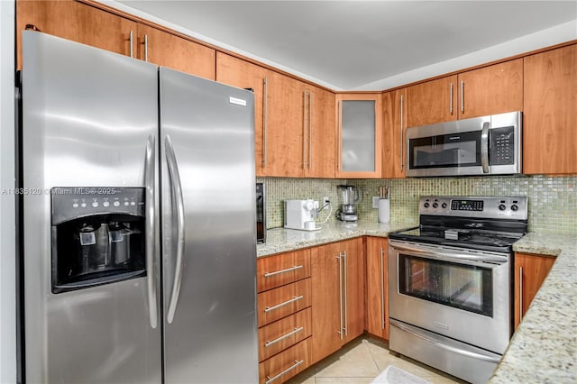 401 Ocean Dr Unit 1024, Miami Beach, FL 33139 - kitchen with stainless steel appliances, brown cabinets, decorative backsplash, light stone counters, and glass insert cabinets