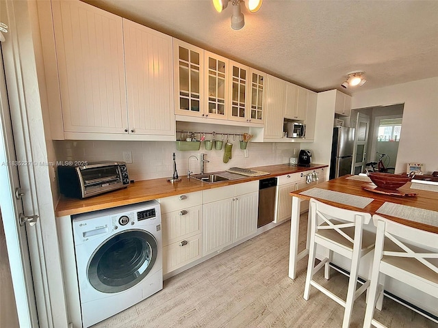 224 Meridian Ave Unit 10, Miami Beach, FL 33139 - kitchen featuring washer / dryer, appliances with stainless steel finishes, decorative backsplash, light wood finished floors, and butcher block counters