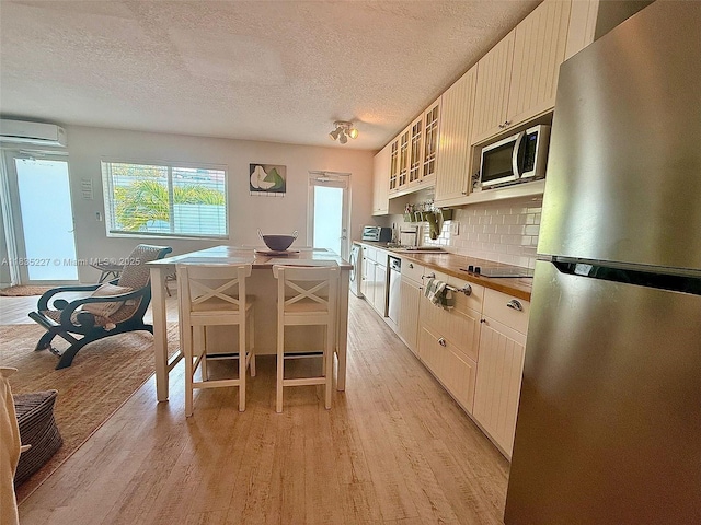 224 Meridian Ave Unit 10, Miami Beach, FL 33139 - kitchen featuring appliances with stainless steel finishes, a textured ceiling, healthy amount of natural light, light wood-style flooring, and decorative backsplash