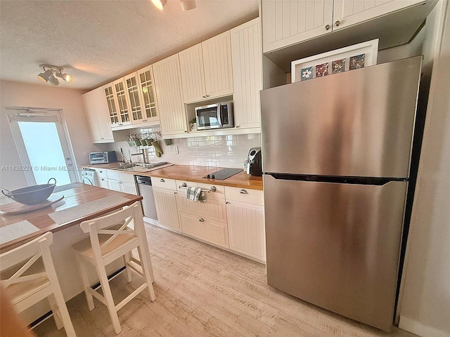 224 Meridian Ave Unit 10, Miami Beach, FL 33139 - kitchen featuring appliances with stainless steel finishes, butcher block counters, light wood-style floors, backsplash, and glass insert cabinets