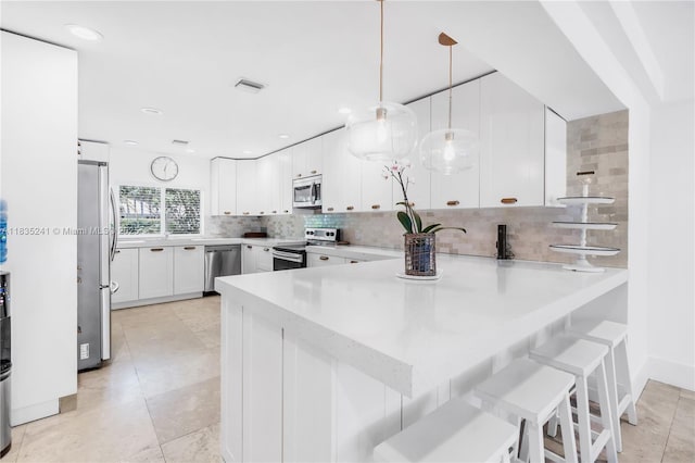10821 SW 92nd Ave, Miami, FL 33176 - kitchen featuring appliances with stainless steel finishes, a peninsula, backsplash, white cabinetry, and pendant lighting