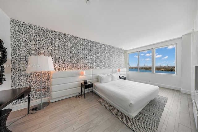 1100 W Ave Unit 1614, Miami Beach, FL 33139 - bedroom featuring wallpapered walls, light wood-style floors, an accent wall, and a water view