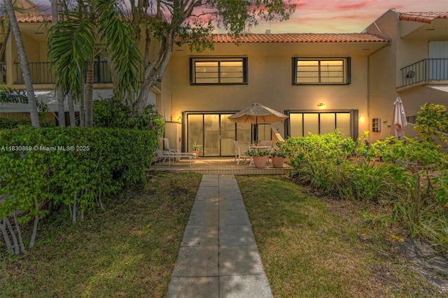 1426 NE 105th St Unit D9, Miami Shores, FL 33138 - back of property at dusk featuring a tiled roof, stucco siding, a patio, and a yard