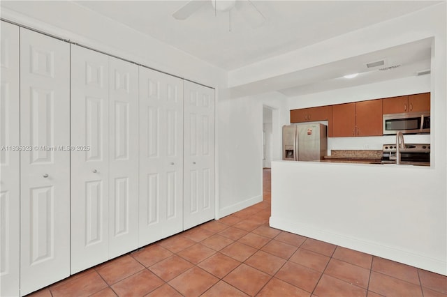 15831 Palmetto Club Dr, Miami, FL 33157 - kitchen featuring appliances with stainless steel finishes, a ceiling fan, light tile patterned flooring, brown cabinets, and a peninsula