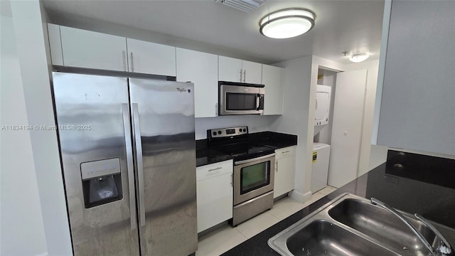 1871 NW S River Dr Unit 1506, Miami, FL 33125 - kitchen with appliances with stainless steel finishes, stacked washer / dryer, dark countertops, white cabinets, and light tile patterned floors