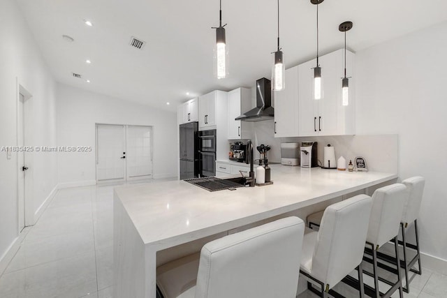 7029 W 29th Way, Hialeah, FL 33018 - kitchen featuring wall chimney range hood, lofted ceiling, light countertops, a peninsula, and a kitchen bar