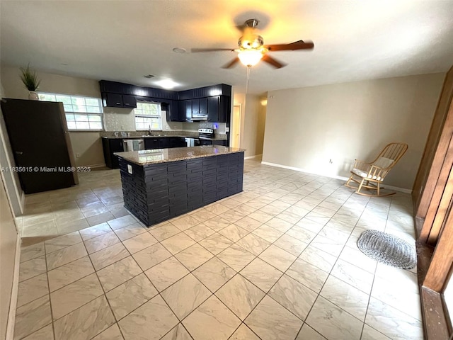 1148 N Singleton Ave, Titusville, FL 32796 - kitchen with stainless steel appliances, dark cabinets, a ceiling fan, dark stone countertops, and a kitchen island