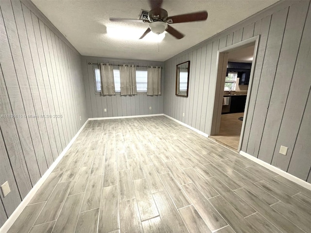 1148 N Singleton Ave, Titusville, FL 32796 - empty room featuring light wood-type flooring, a ceiling fan, wood walls, plenty of natural light, and a textured ceiling