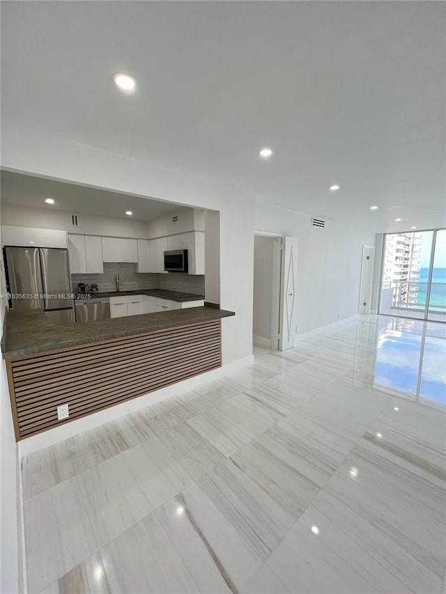 5700 Collins Ave Unit 16B, Miami Beach, FL 33140 - kitchen with appliances with stainless steel finishes, dark countertops, open floor plan, white cabinets, and decorative backsplash