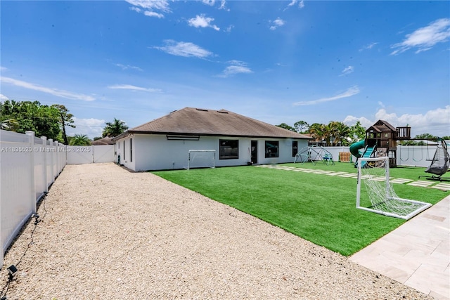 1149 SE Sandia Dr, Port St Lucie, FL 34983 - back of property with a playground, a fenced backyard, a shingled roof, stucco siding, and a patio