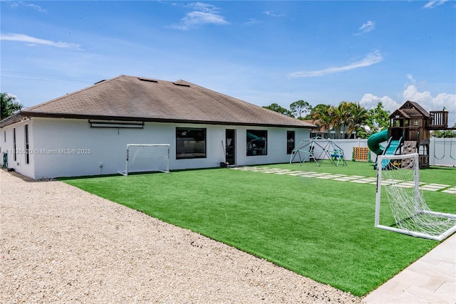 1149 SE Sandia Dr, Port St Lucie, FL 34983 - back of property with a playground, roof with shingles, and stucco siding