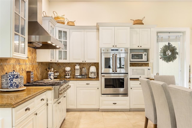 7245 SW 104th St, Pinecrest, FL 33156 - kitchen with stainless steel appliances, wall chimney range hood, light tile patterned floors, backsplash, and white cabinetry