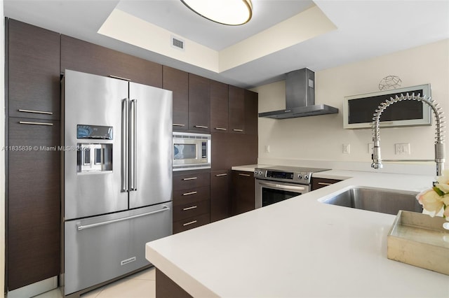 150 Sunny Isles Blvd Unit 1-1401, Sunny Isles Beach, FL 33160 - kitchen with stainless steel appliances, wall chimney exhaust hood, dark brown cabinets, light countertops, and a tray ceiling